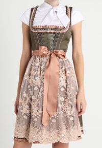 Vestido dirndl tradicional con corpiño oliva, cintas rosa y lazo, blusa blanca y falda de delantal bordada con flores en color beige.