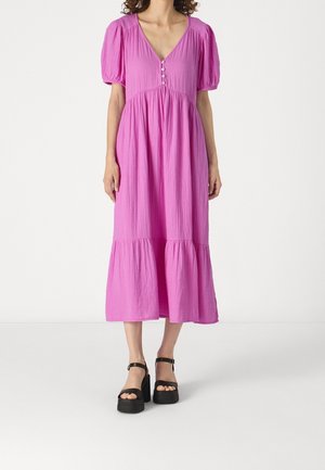 Vestido midi rosa con escote en V y mangas abullonadas, con un detalle de botones en la parte superior y un dobladillo con volantes. Combinado con sandalias de plataforma negras.