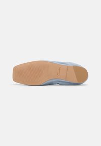 Semelle d'une chaussure plate bleu clair avec une semelle en caoutchouc beige présentant une adhérence texturée et le nom de la marque "Clarks" sur la zone de la voûte plantaire.
