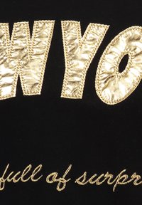 Un tejido negro presenta grandes letras doradas brillantes que deletrean "WYOMING" con un acabado texturizado, y un texto más pequeño en cursiva que dice "lleno de sorpresas".