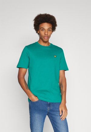 Groene crewneck t-shirt van katoen, met korte mouwen en een klein geel logo op de linkerkant van de borst. Gepaard met blauwe jeans.