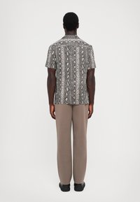 Chemise à manches courtes avec un motif en imprimé serpent en gris et noir, associée à un pantalon beige. Tissu lisse, coupe décontractée, col simple.
