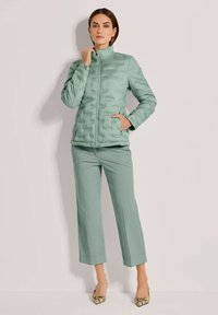 Hellgrüne Pufferjacke mit hohem Kragen und gesteppter Textur, kombiniert mit passenden Hosen und gemusterten Absätzen.