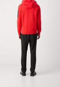 Röd huvtröja med ribbade muddar, tillsammans med svarta byxor. Tyget ser mjukt ut, med en slät yta och minimal hårdvara.