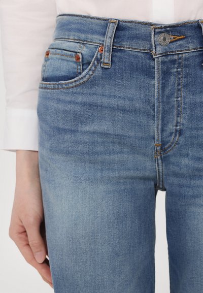 Jeans de mezclilla azul claro con un diseño clásico, cinco bolsillos, costuras notables y un cierre de botón metálico en la cintura.