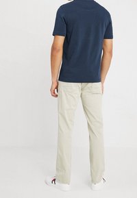 Camiseta de manga corta azul marino combinada con pantalones beige claros. Zapatillas blancas con acentos rojos y azules visibles en los zapatos. Atuendo casual.