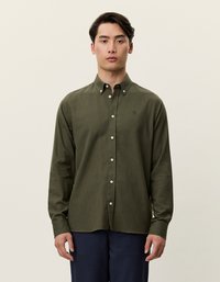 Mørk grønn langermet skjorte med krage som knappes, med en subtil tekstur, hvite knapper og en liten logo på brystet.