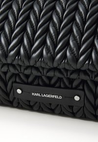 Black leather handbag featuring a braided texture, smooth finish, and a rectangular shape. Includes a silver logo tag and details.