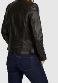 Giubbotto di pelle nera con un design attillato, dettagli delle cuciture visibili e pannello posteriore testurizzato, abbinato a jeans blu scuro.