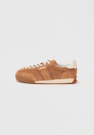 Brązowy zamszowy sneaker Polo z perforowanymi panelami, białymi sznurowadłami i kremową podeszwą, pokazany z profilu na szarym tle.