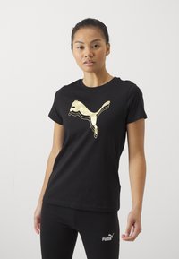 Tricou din bumbac negru cu un logo mare Puma de culoare aurie pe față. Mâneci scurte și un design clasic cu guler rotund. Stil ajustat.