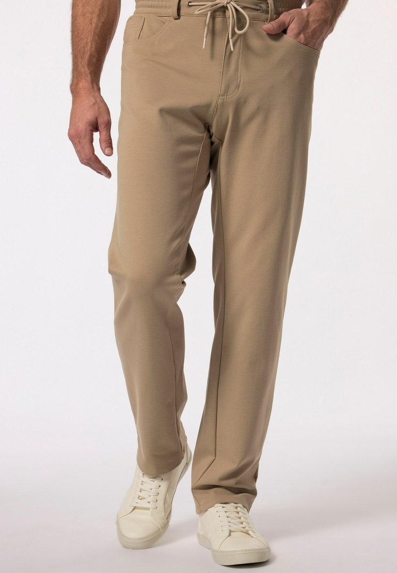 Beżowe spodnie elastyczne w pasie z sznurkiem, bocznymi kieszeniami i gładką teksturą. W zestawie z białymi sneakersami.