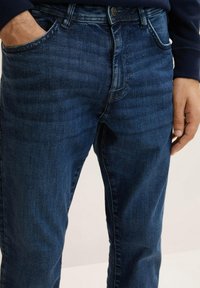 Jeans din denim albastru închis cu un finisaj texturat, design clasic cu cinci buzunare și închidere cu buton vizibil la talie.