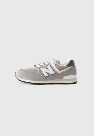Baskets New Balance grises et beiges avec des lacets blancs et un tissu texturé, vues de côté sur un fond clair uni.