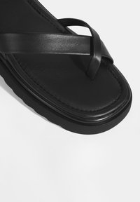 Zwarte leren flip-flopsandalen met kruisbanden, een gestructureerde voetbed en een dikke, ronde rubberen zool.