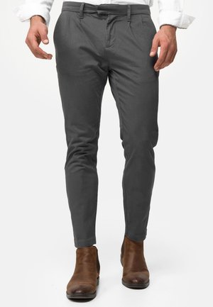 Pantalones gris ajustados de corte entallado, con pliegues frontales y bolsillos laterales, combinados con botas cortas marrones.
