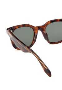 Occhiali da sole tartarugati con lenti verdi. Forma a occhio di gatto con finitura liscia e lucida, e una sottile asticella rastremata con un logo.