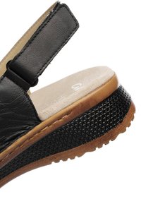 Black leather sandal with a textured rubber sole, adjustable strap, and a beige cushioned footbed. Overall, a low-profile design.
