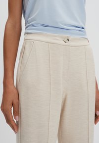 Beige gebloemde broeken met een gestructureerd weefsel, voorzien van twee plooien, zijzakken en een enkele knoopsluiting in de taille.