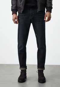 Mörka denimjeans med slim fit, med subtila slitningar och uppvikta ärmar, tillsammans med mörka mockalace-up stövlar.