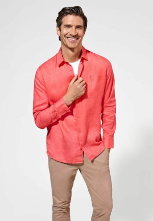 Koralkowa lniana koszula zapinana na guziki z długimi rękawami, z jedną kieszenią na piersi i luźnym krojem, zestawiona z jasnobeżowymi spodniami.