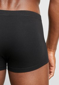 Black cotton boxers feature a smooth texture, snug fit, and a stitched waistband, emphasizing a minimalist design without logos or patterns.