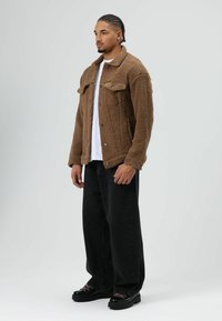 Brown fleece jacket with textured exterior, two chest pockets, and black buttons, paired with black wide-leg pants and chunky black shoes.