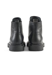 Botas de tobillo de cuero negro con un acabado liso, punteras redondeadas, suelas texturizadas y lengüetas en el talón para ponerlas y quitarlas fácilmente.