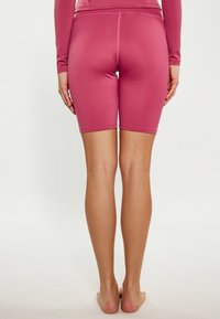 Pantaloni sportivi rosa aderenti con una texture liscia, che arrivano a metà coscia, caratterizzati da un design semplice e cuciture a vista.
