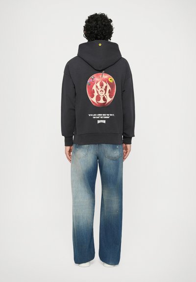 Felpa nera con un grande grafico di una mela rossa infuocata e testo sul retro, abbinata a jeans a gamba larga di colore blu chiaro.