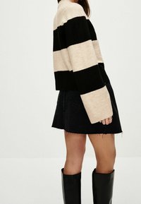 Black and beige striped sweater with a crew neck and ribbed cuffs, paired with a black denim skirt with frayed hem and knee-high black boots.