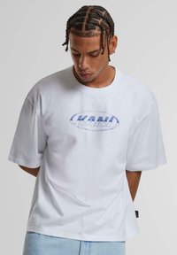 White cotton t-shirt with short sleeves, featuring a blue oval logo "KANI" on the front. Relaxed fit with a straight hem.