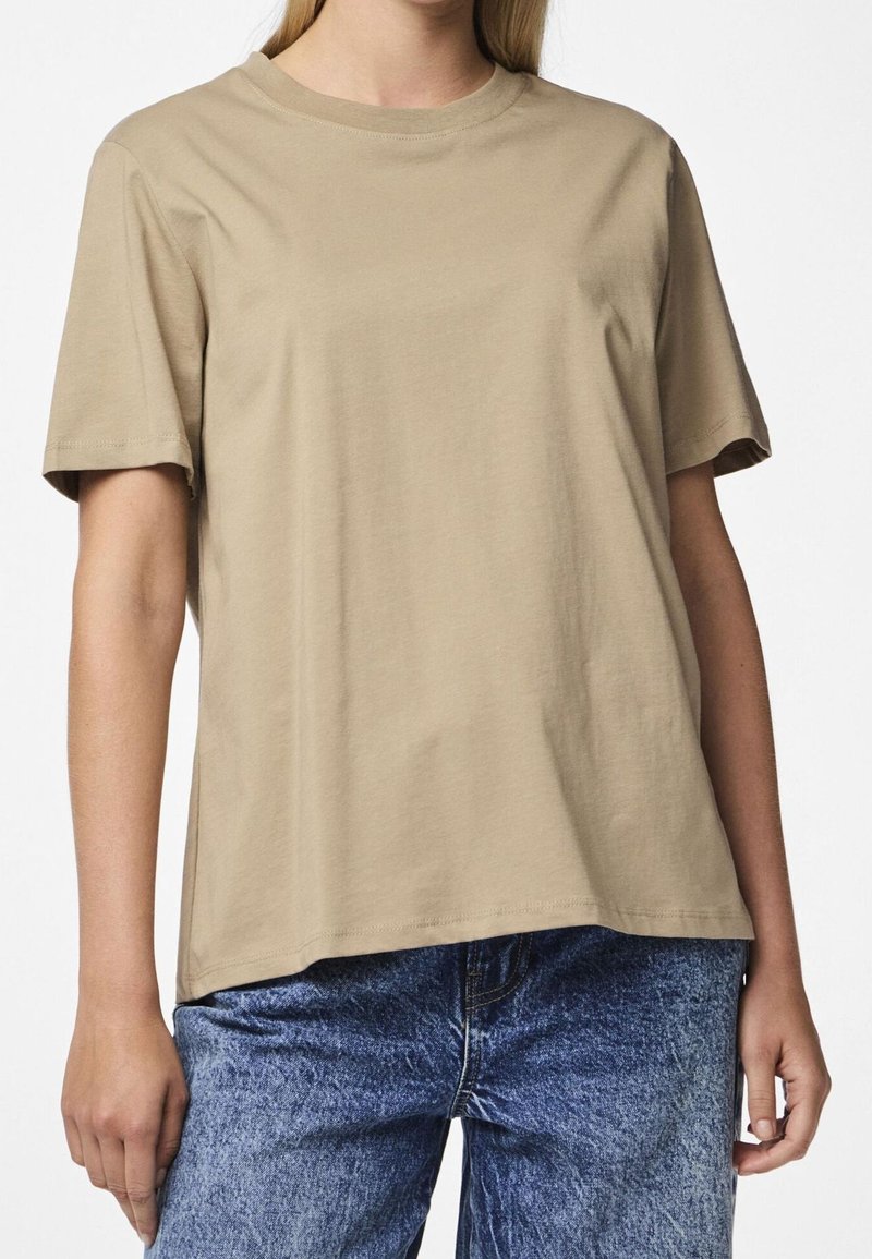T-shirt en coton couleur beige avec un col rond et des manches courtes, présentant une coupe décontractée. Associé à un jean en denim bleu.