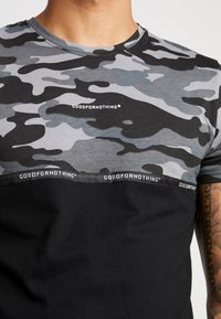 Kurzarm-T-Shirt mit einem grauen Camouflage-Muster und einem schwarzen unteren Bereich. Mit "GOODFORNOTHING"-Logo auf der Brust und am Saum.