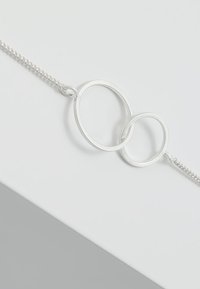 Pulsera de cadena de plata con dos lazos circulares entrelazados, uno ligeramente más pequeño que el otro, con un acabado texturizado.