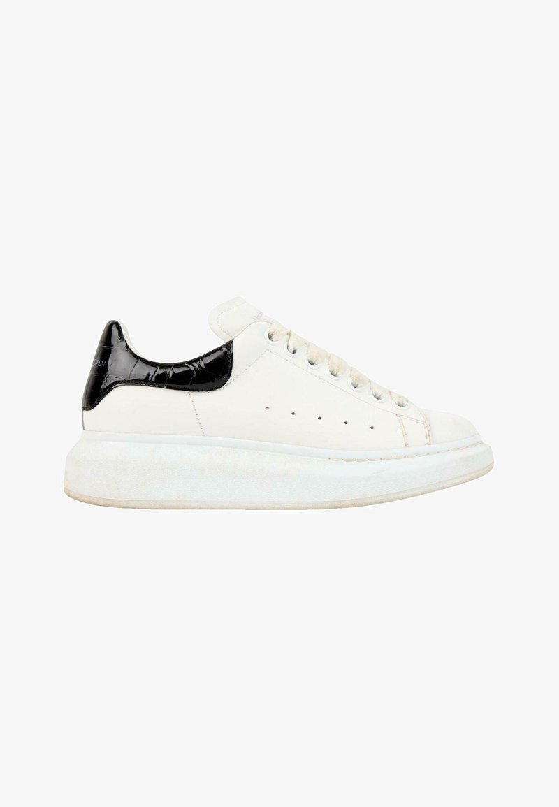 Baskets basses blanches avec languette de talon noire texturée, lacets blancs et semelle blanche épaisse, vues de l'extérieur.