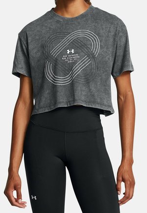 Femme portant un T-shirt court gris Under Armour avec un motif blanc entrelacé représentant une piste et le texte « Run Anywhere Run Everywhere », associé à un legging noir.