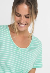T-shirt a righe verde chiaro con scollo a barchetta, caratterizzato da un piccolo fiocco verde vicino al colletto. Tessuto morbido in cotone con una vestibilità morbida.