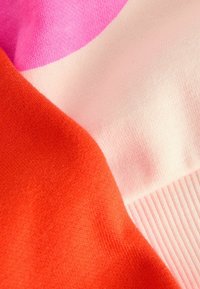 Weicher Strickstoff mit Farbblocken in leuchtendem Pink, Orange und zartem Pfirsich, der Textur und gerippten Kantendetails zeigt.