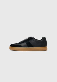 Black sneakers made of leather and suede, featuring a gum sole, lace-up design, and a side panel accent. Simple, modern shape.
