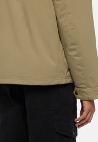 Khaki padded jacket with a smooth texture, featuring a rounded hem and snap-button cuff, paired with black cargo pants.