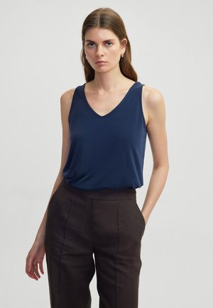 Top sin mangas de color azul marino con escote en V, hecho de un tejido suave, combinado con pantalones oscuros de corte entallado que presentan pliegues ordenados.