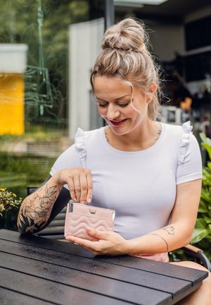 Light pink wallet made of textured material with a wavy design and silver hardware, held by a person seated at a wooden table.