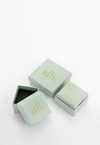 Trois boîtes à bijoux carrées vert clair avec des logos dorés "elli premium", une ouverte montrant un intérieur noir, disposées sur un fond blanc.