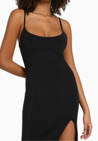 Robe noire sans manches avec un décolleté arrondi et une fente haute jusqu'à la cuisse. Fabriquée en tissu lisse et extensible avec des bretelles fines et une silhouette ajustée.