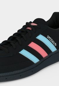 Baskets noires avec des rayures roses et bleu clair, lacets noirs et marquage "SPEZIAL" sur le côté.