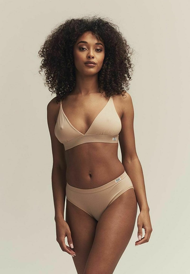 Brassière beige et culottes assorties en tissu doux. La brassière présente un design en V avec des bretelles réglables. Étiquette de marque minimaliste visible.