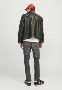 Veste en cuir noire avec un col plat, portée sur une chemise blanche, associée à un jean gris foncé et des chaussures noires avec des accents blancs. Casquette rouge.