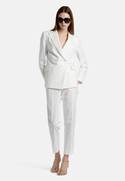 Witte dubbelzijdige blazer met spitse revers, gecombineerd met op maat gemaakte witte broeken. Draag met zwarte zonnebril en gouden sandalen met bandjes.