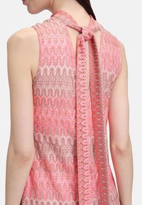 Rosa gestricktes Kleid mit wellenförmigen Mustern, offener Rückseite und einer Schleife am Hals. Der Stoff hat eine strukturiert Oberfläche.